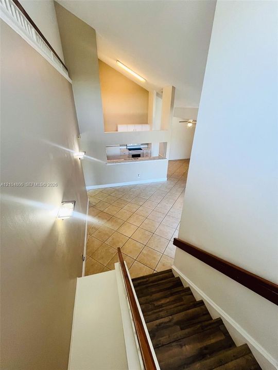 Vaulted ceilings, wood-finish stair treads, tile flooring, built-in kitchen cabinetry, and a ceiling fan