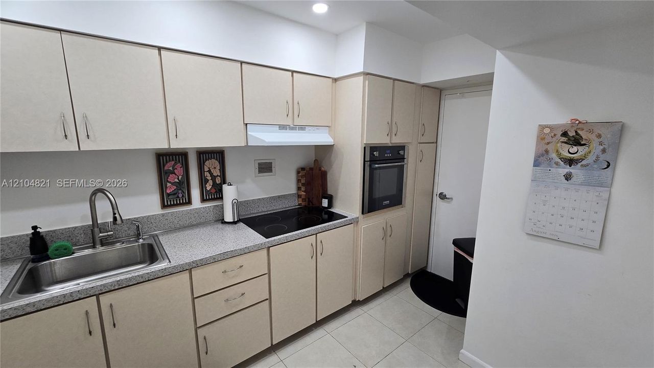 Kitchen featuring extensive light-toned cabinetry, built-in oven, integrated electric cooktop, stainless steel sink with a high-arc faucet, and light-colored countertops