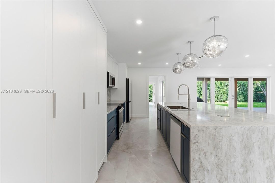 Kitchen featuring floor-to-ceiling cabinetry, a stone-top waterfall island, modern pendant lighting, deep-toned base cabinetry, and large-format tile flooring