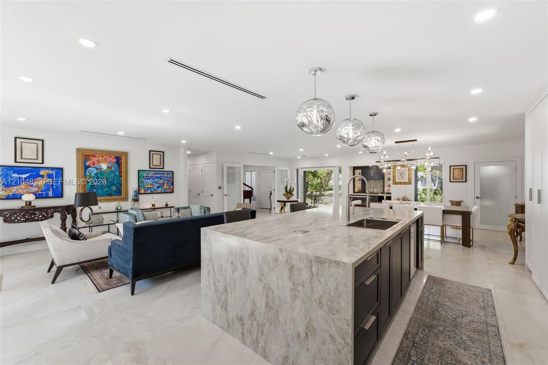 Expansive open-concept living space featuring a large kitchen island with integrated sink, white tile flooring, recessed lighting, and multiple pendant light fixtures