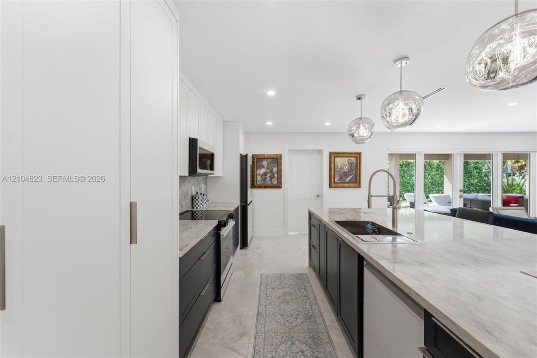 Contemporary kitchen featuring an expansive island with an undermount sink, pendant lighting, built-in appliances, and white flat-panel cabinetry