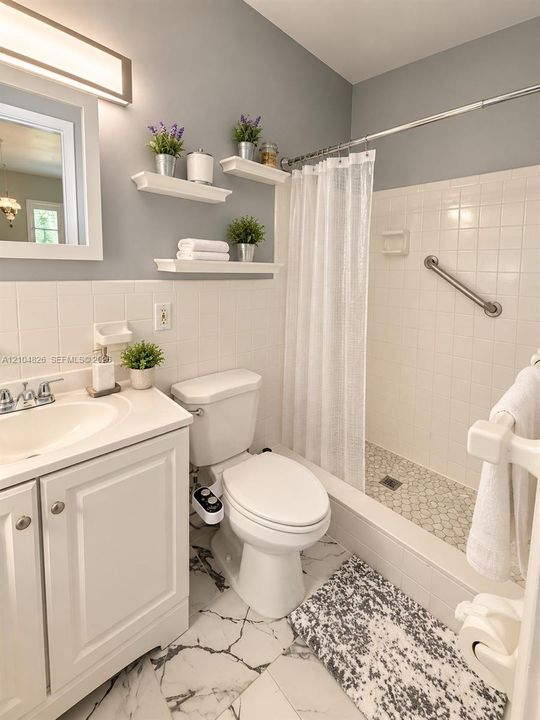 White tile wainscoting and bath surround, white vanity with integrated sink, floating wall shelving, white subway tile shower, and a pebble tile shower floor