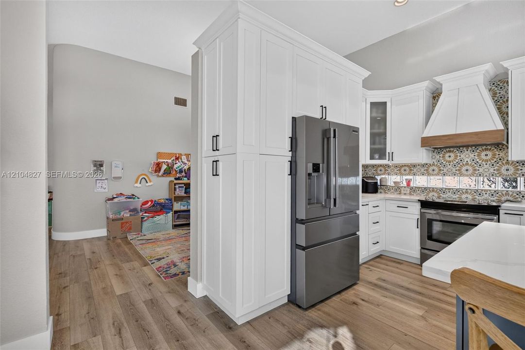 Kitchen featuring white shaker-style cabinetry, floor-to-ceiling built-in pantry, wood-finish flooring, patterned tile backsplash, and stainless-steel appliances