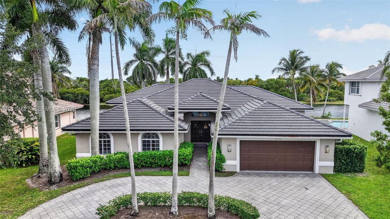 Single-story residence featuring a tile roof, paved circular driveway, arched windows, and mature palm trees