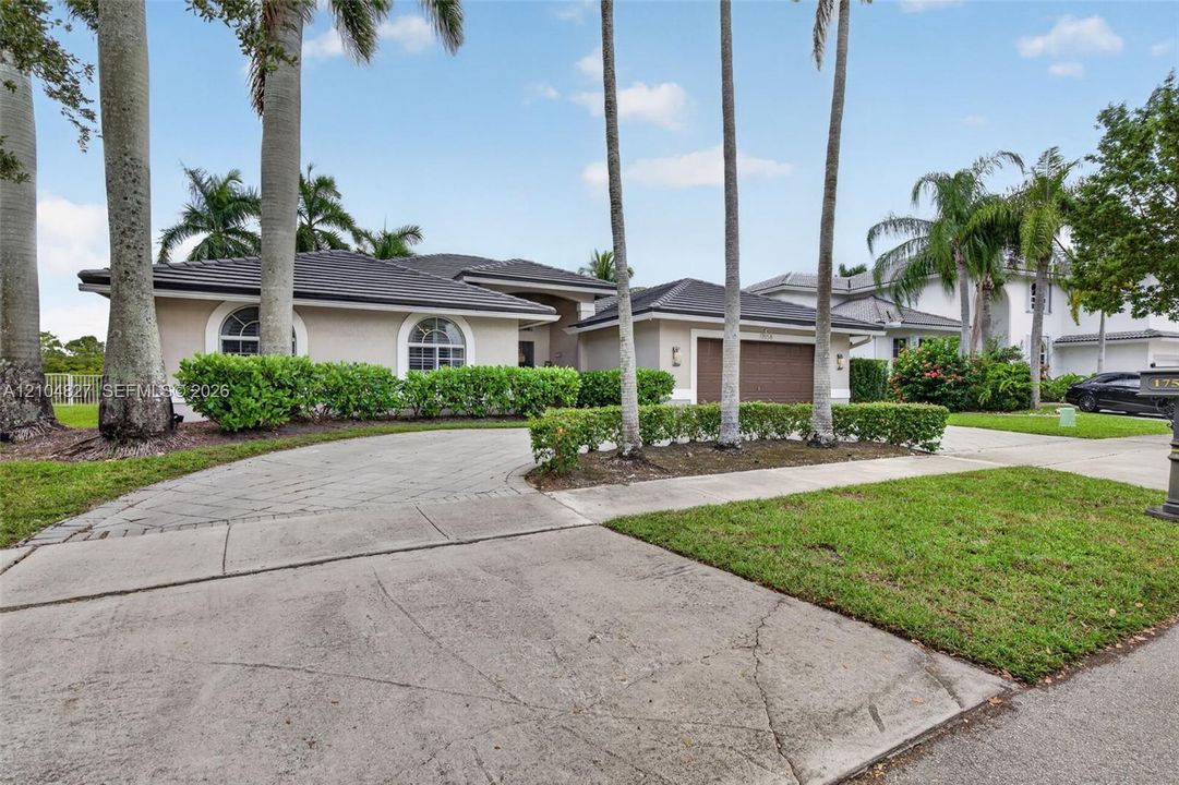 Stucco exterior residence featuring a multi-hipped tile roof, arched windows, and a paved stone driveway leading to an attached garage