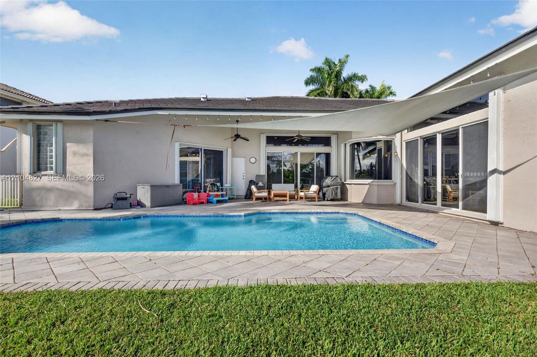 Outdoor space featuring a swimming pool, stone-paver patio, shaded canopy, and sliding glass door access