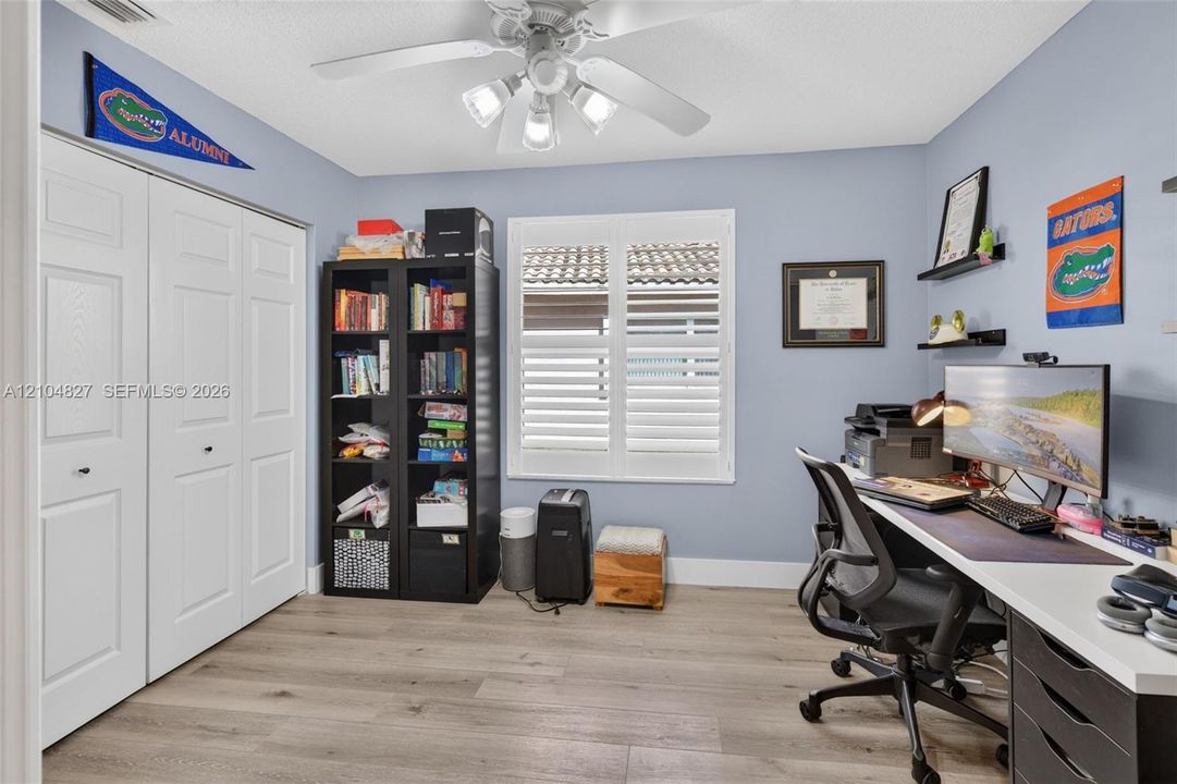 Wood-finish flooring, white bifold closet doors, plantation shutters, and a multi-light ceiling fan