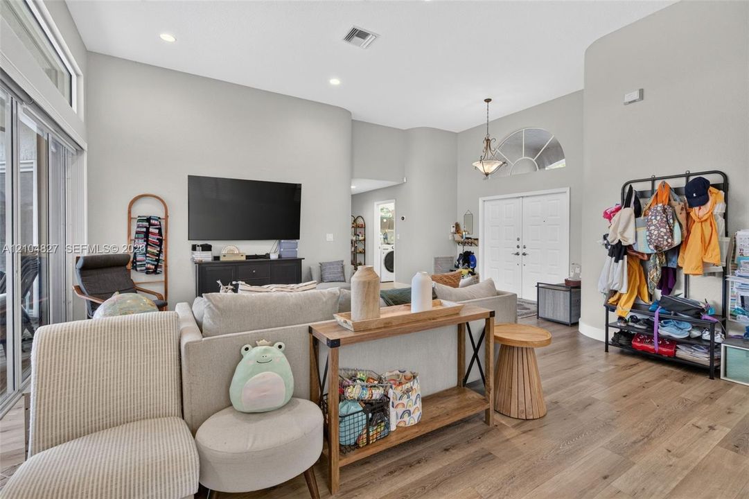 Open-concept interior featuring high ceilings, wood-finish flooring, recessed lighting, double-door entry with arched transom window, and sliding glass doors