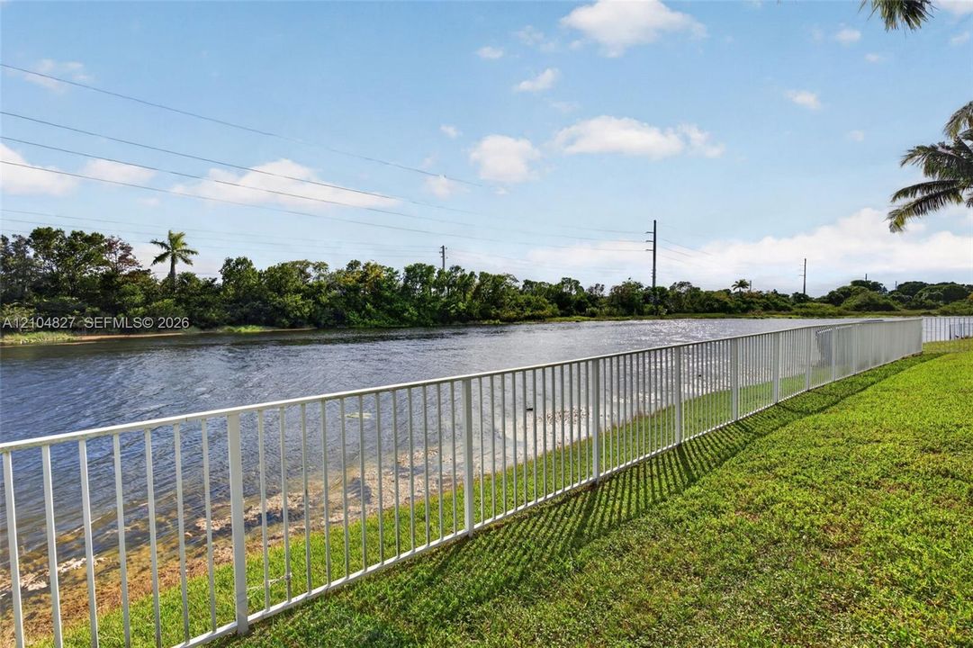 Waterfront lot featuring a manicured lawn and white metal perimeter fencing