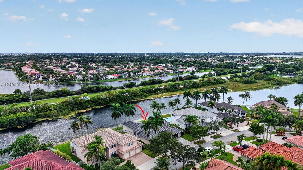 Aerial perspective of a waterfront property featuring a canal-side location, mature palm trees, a private swimming pool, and a shingled roof
