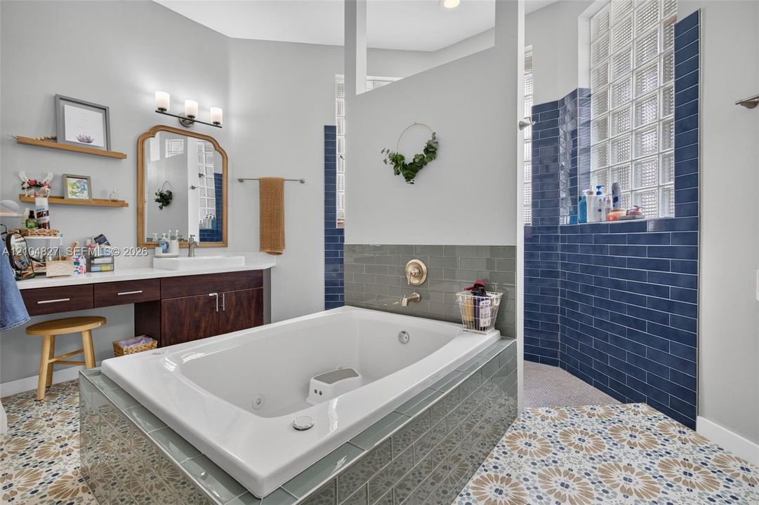 Soaking tub with a tiled surround, patterned floor tile, dark wood-finish cabinetry, glass block windows, and wall-mounted light fixtures
