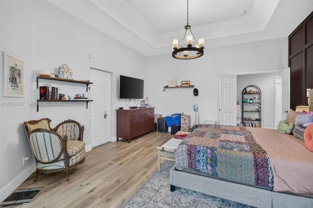Tray ceiling featuring a central multi-light chandelier, dark-toned wood-panel accent wall, and wood-finish flooring