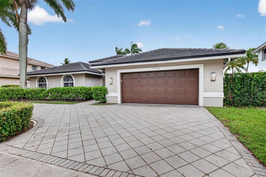 Stucco exterior featuring a dark-toned tile roof, paved diamond-pattern driveway, oversized two-car garage, and arched windows