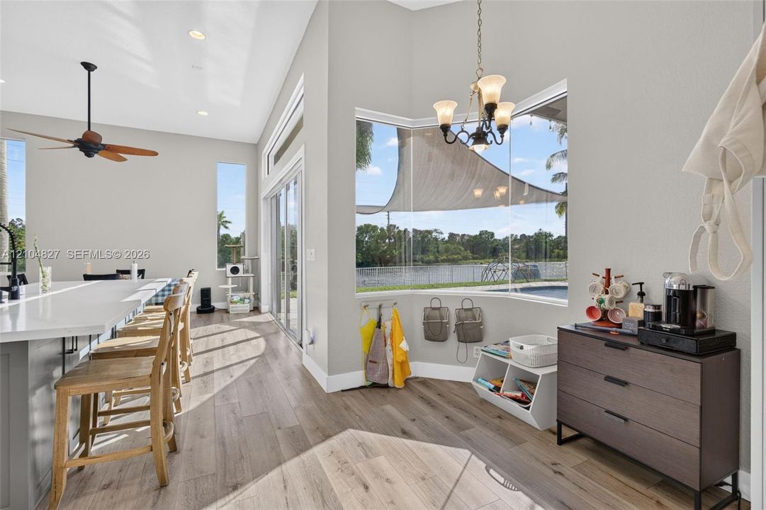 Open-concept interior featuring wood-finish flooring, a kitchen island with stone countertops, a bay window with water and pool backdrop, a multi-light chandelier, and recessed lighting