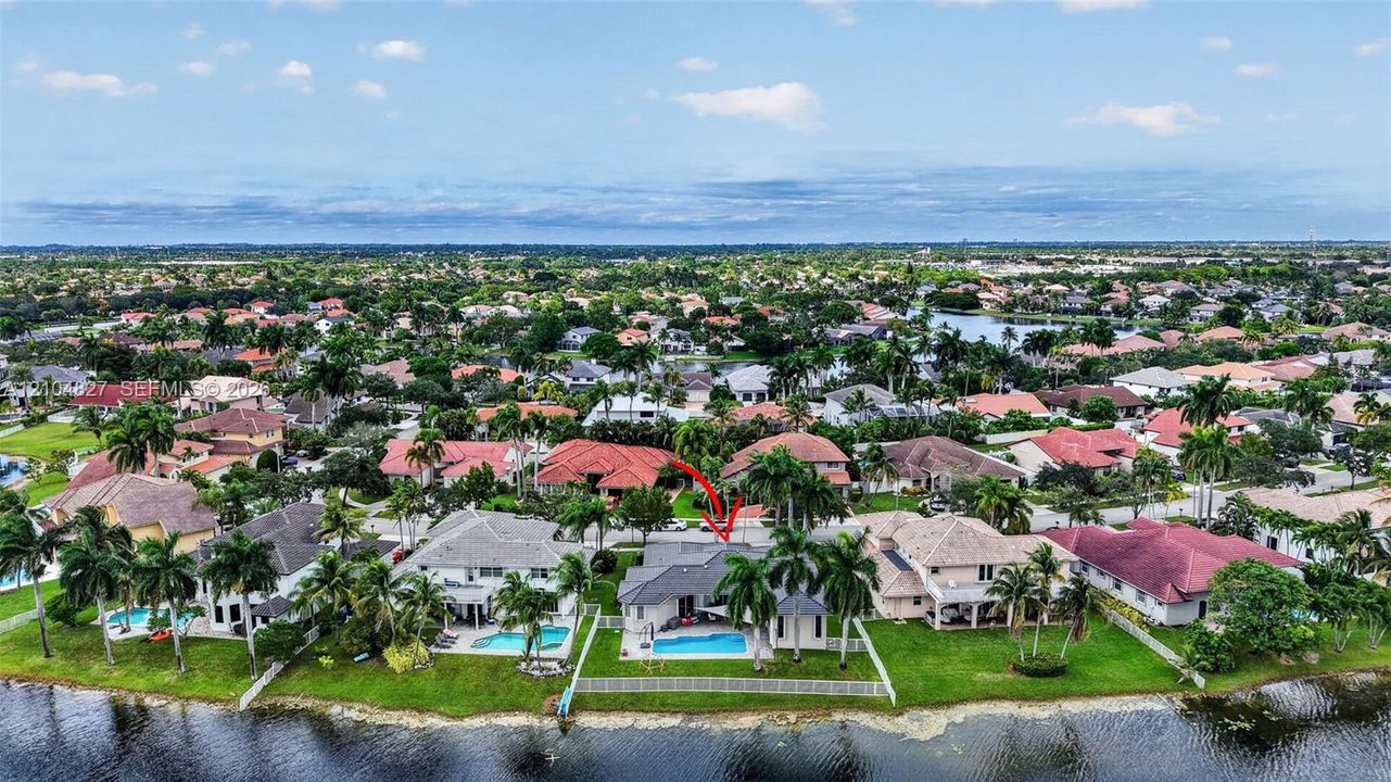 Aerial view featuring a waterfront property with an in-ground swimming pool, tile roofing, and mature palm trees