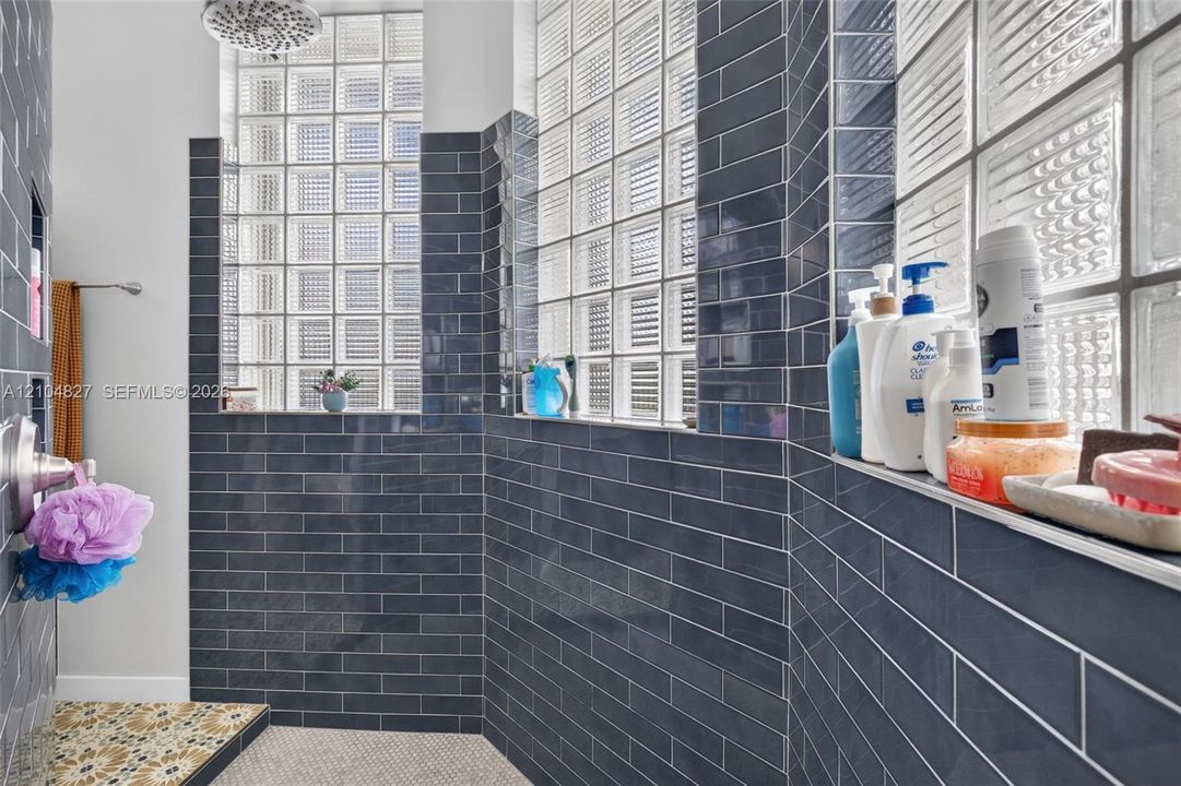 Walk-in shower featuring dark blue subway-style wall tile, integrated glass block windows, a built-in recessed shelf, and a rainfall showerhead
