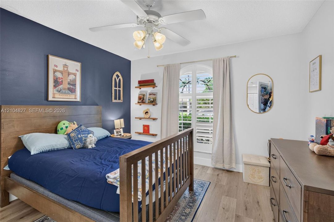 Room featuring wood-finish flooring, an arched window with interior shutters, a bold navy accent wall, and a ceiling fan with integrated lighting