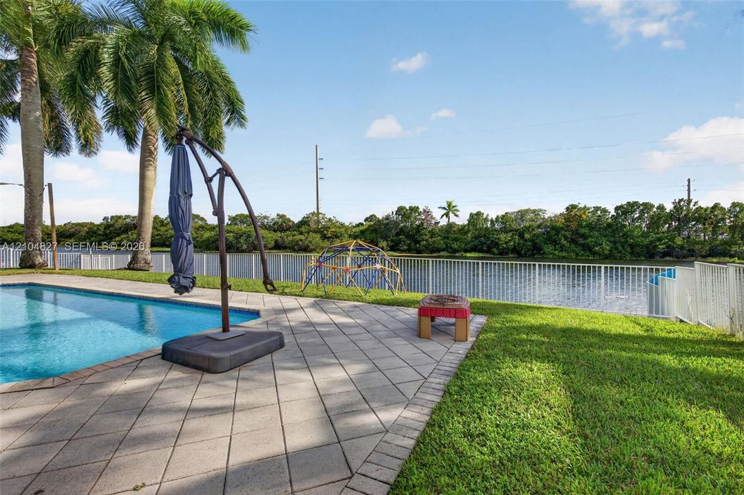 Backyard featuring a concrete paver patio, in-ground swimming pool, manicured lawn, metal perimeter fencing, and waterfront positioning