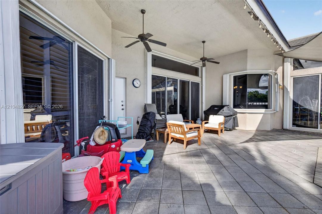 Covered patio featuring tiled flooring, two ceiling fans, and large glass sliding doors