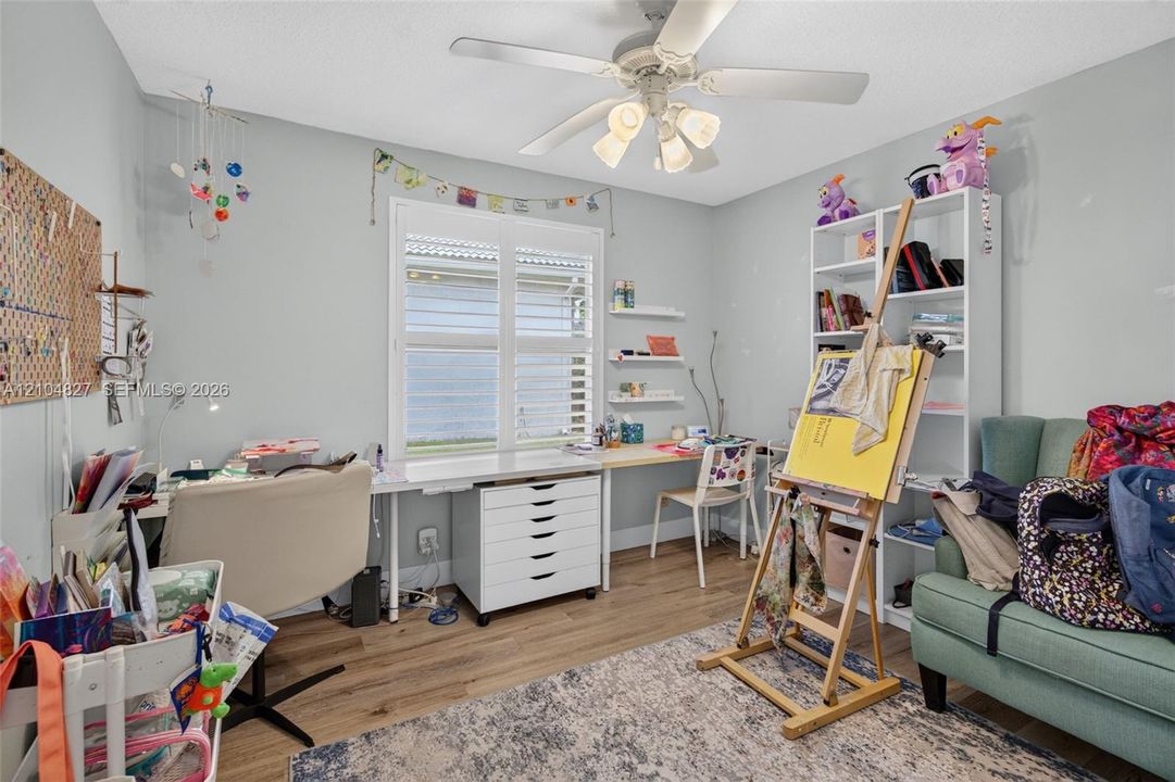 Room featuring wood-finish flooring, plantation shutters, built-in shelving, and a ceiling fan with multi-directional lighting