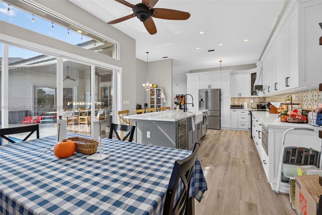 Kitchen featuring shaker-style cabinetry, large center island with integrated wine storage, farmhouse-style sink, patterned tile backsplash, and wood-finish flooring