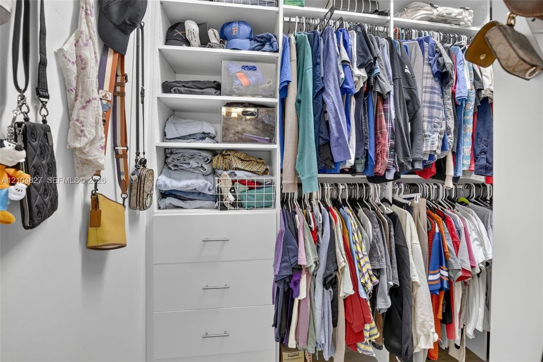 Custom reach-in closet featuring white built-in shelving, multiple hanging rods, and a stack of three integrated storage drawers with minimalist hardware
