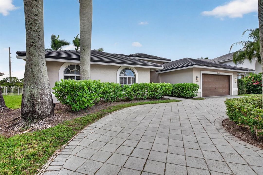 Single-story residence featuring a tile roof, arched windows, concrete paver driveway, and an attached multi-car garage