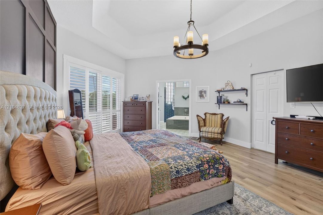 Tray ceiling, wood-finish flooring, dark-toned board and batten accent wall, multi-tiered metal chandelier, and plantation shutters