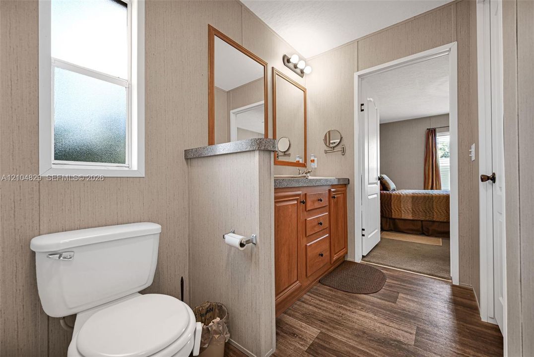 Bathroom featuring wood-finish flooring, a wood vanity with a stone-finish countertop, dual wall-mounted mirrors, and a frosted glass window