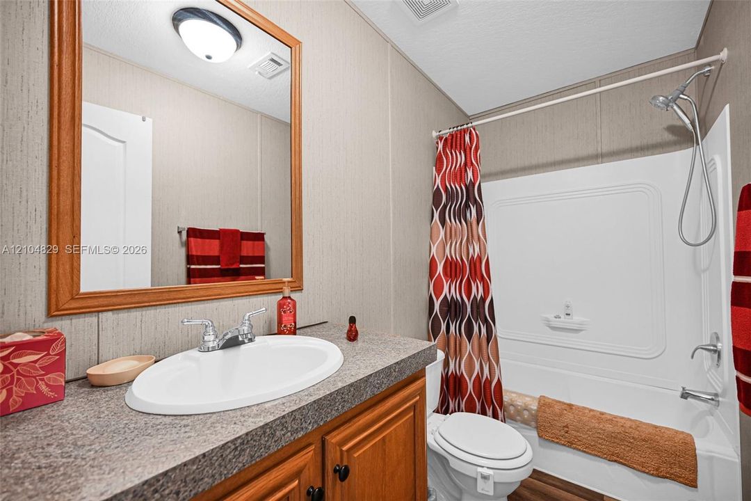 Bathroom featuring a wooden vanity, a stone-finish countertop with an inset oval sink, a large wood-framed mirror, and a tub-shower combination
