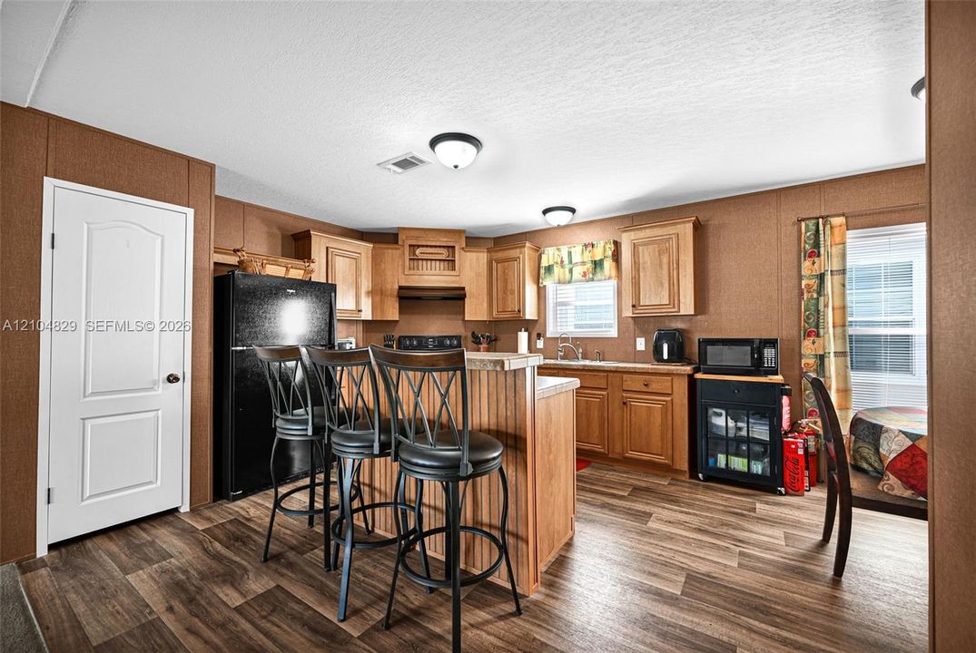 Kitchen featuring wood-finish cabinetry, a central breakfast bar, wood-finish flooring, dual flush-mount ceiling lighting, and a solid-panel door