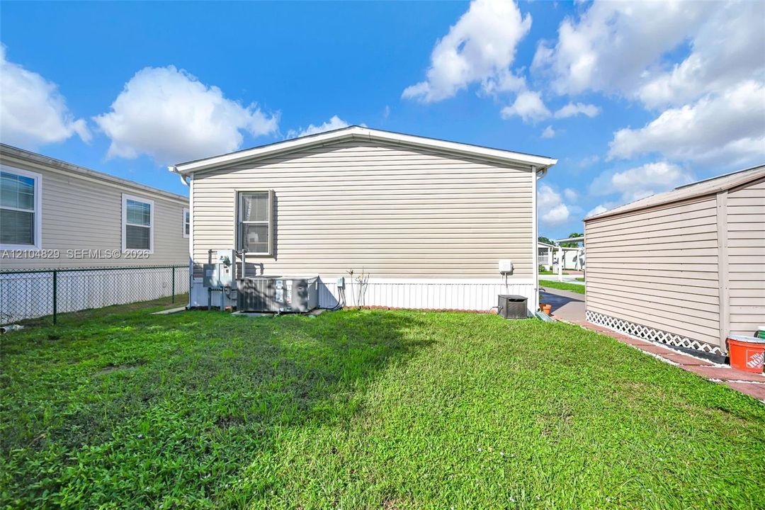 Exterior featuring light-toned horizontal siding, central air conditioning unit, chain-link fencing, and turf-covered yard area