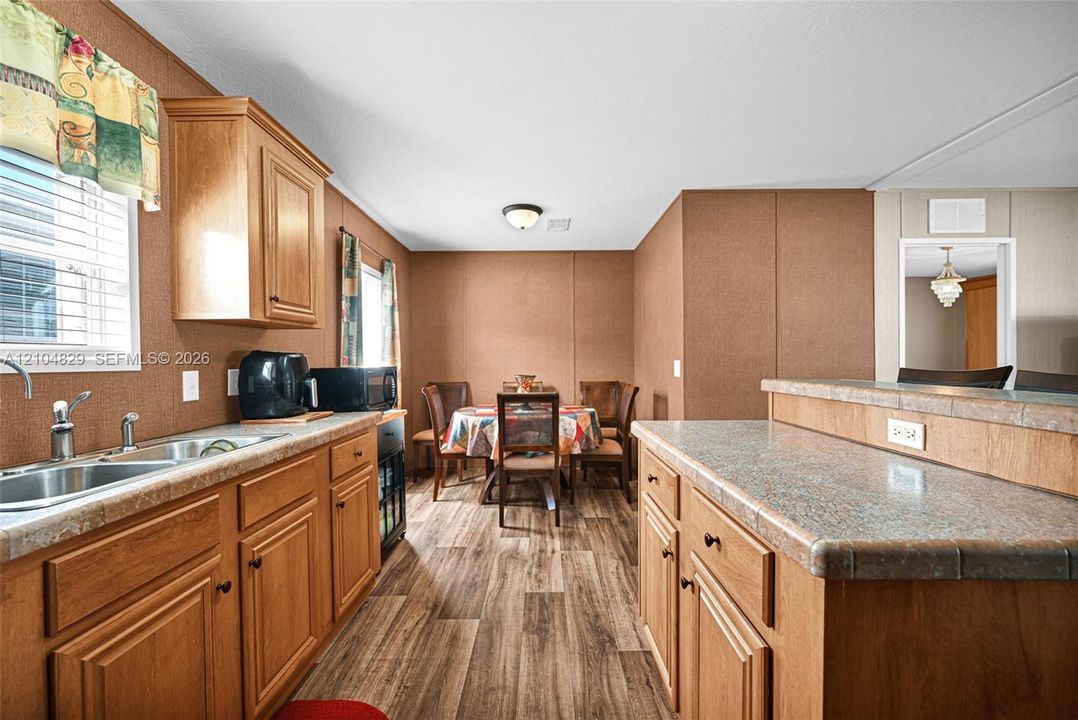 Kitchen area featuring wood-finish cabinetry, laminate countertops, a dual-basin sink, and wood-finish flooring