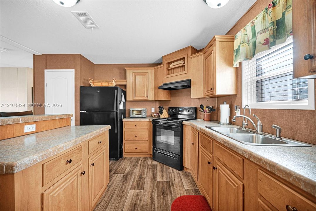 Kitchen featuring wood cabinetry, laminate countertops, a double-basin stainless steel sink, wood-finish flooring, and black appliances