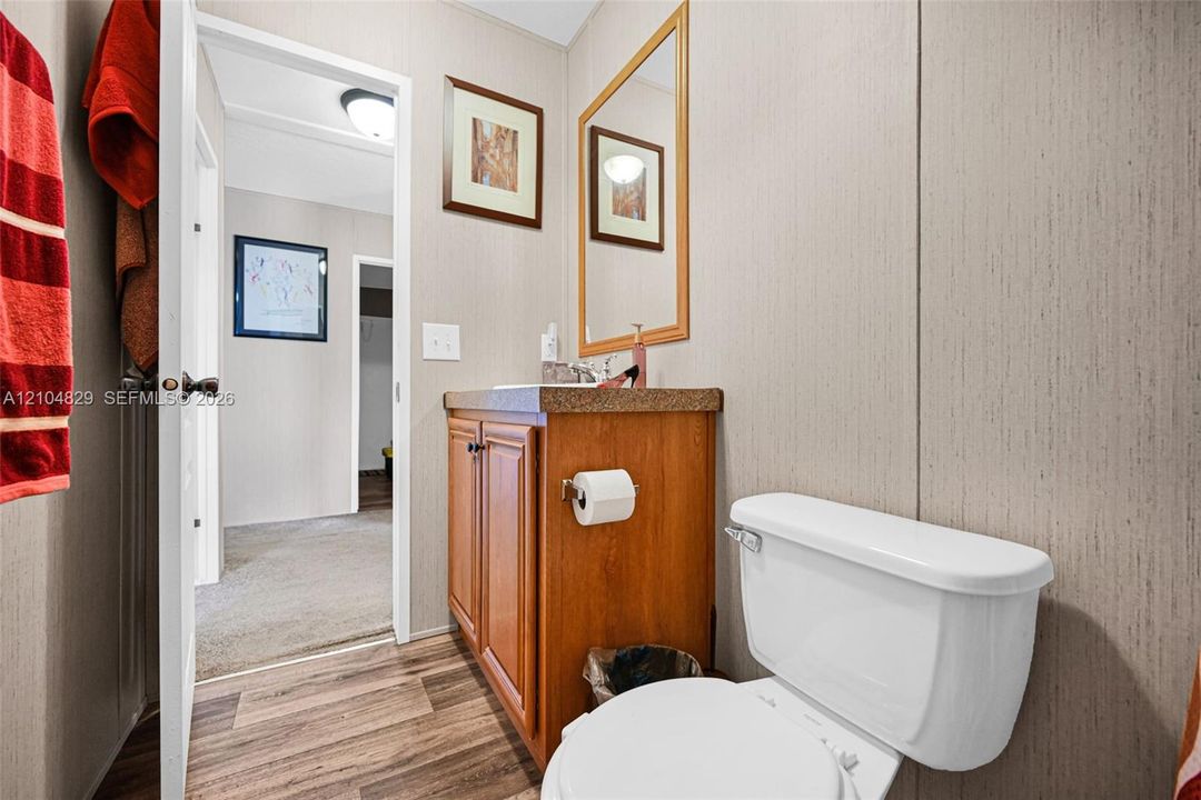 Bathroom featuring wood-finish cabinetry, a textured countertop, a wall-mounted mirror with a wood frame, and wood-finish flooring