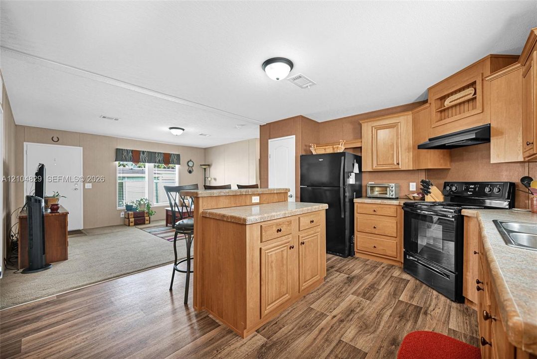Kitchen featuring wood-finish cabinetry, a central island with storage, stone-patterned countertops, and black appliance suite