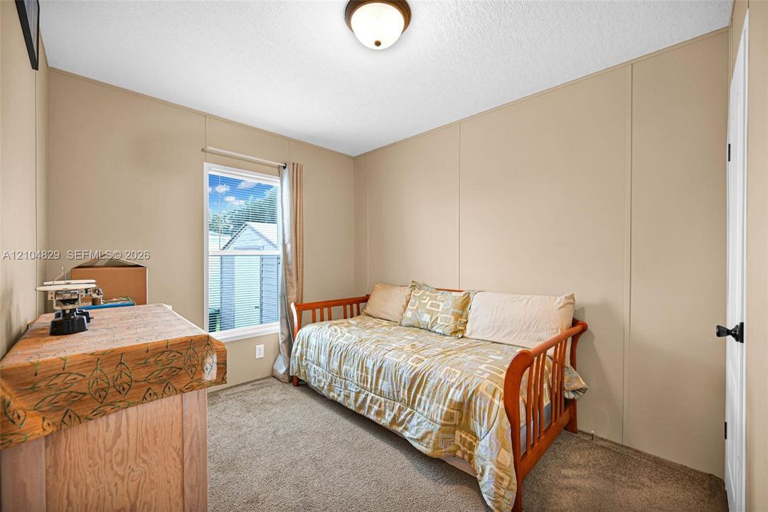 Neutral-toned wall panels, carpeted flooring, single-pane window, and a centered flush-mount ceiling light fixture