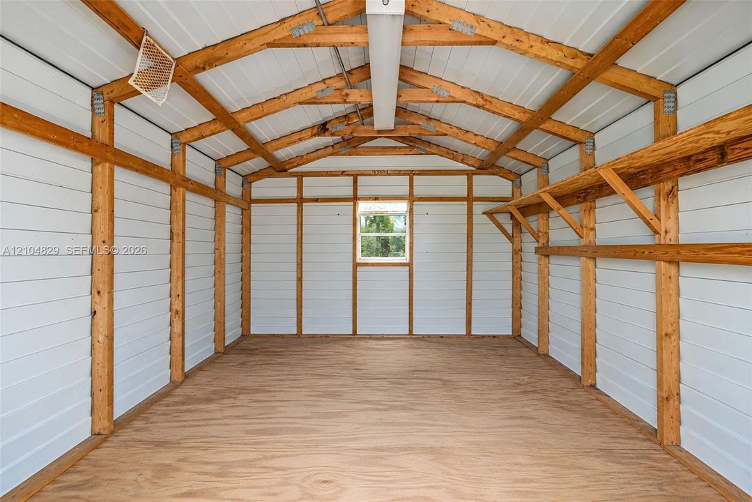 Exterior storage structure featuring exposed timber framing, white paneled walls, plywood flooring, integrated wall-mounted shelving, and a single window