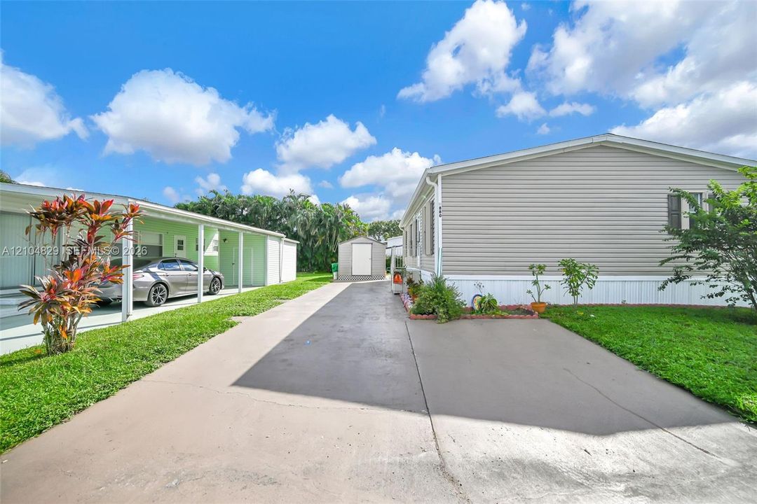 Horizontal siding exterior with a concrete driveway, covered parking area, and detached storage shed