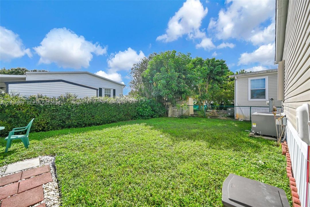 Side yard featuring a grass lawn, perimeter shrubbery, and chain-link fencing