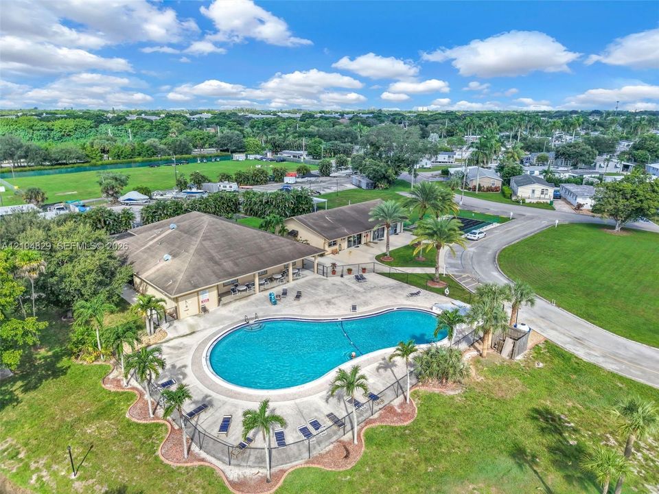 Community center featuring a kidney-shaped swimming pool, concrete pool deck, enclosed perimeter fencing, and established palm landscaping