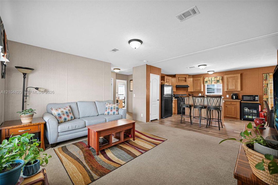 Open-concept interior featuring wood-finish flooring, natural wood cabinetry, flush-mount ceiling lighting, and a kitchen island with bar-style seating