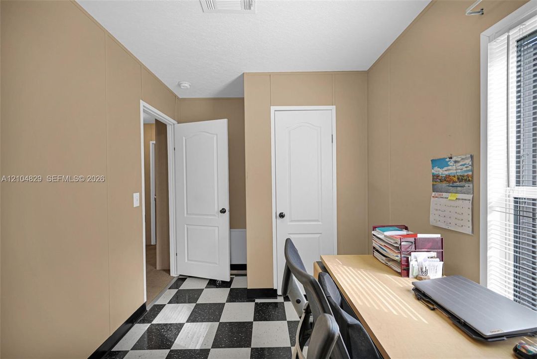 Interior room featuring checkered vinyl flooring, two white panel doors, and a window with horizontal blinds