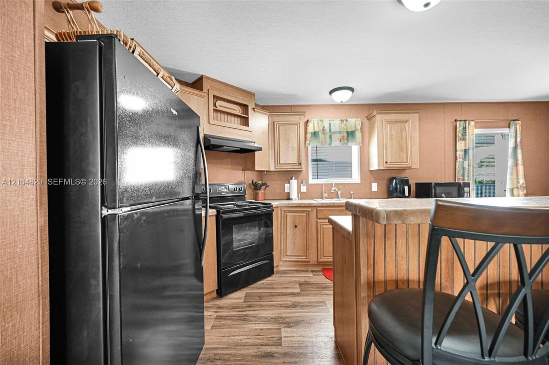 Kitchen featuring wood-finish cabinetry, black appliance package, wood-finish flooring, and a breakfast bar with a solid surface countertop
