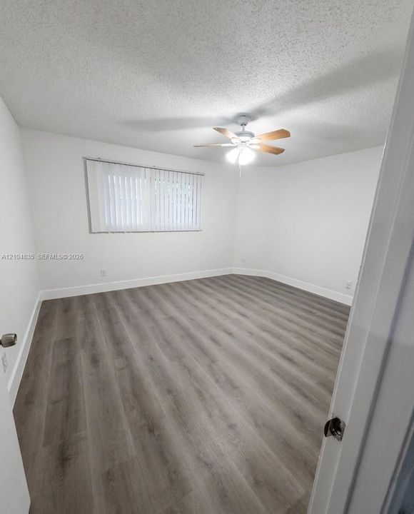 Interior room featuring wood-finish flooring, white walls, and a ceiling-mounted light fixture with a multi-blade fan