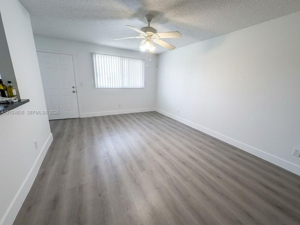 Room featuring wood-finish flooring, a ceiling fan with integrated lighting, and vertical blinds