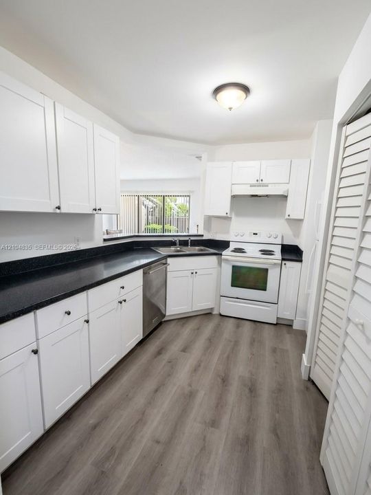 Kitchen featuring white shaker-style cabinetry, dark stone-finish countertops, wood-finish flooring, a stainless steel dishwasher, and a white range