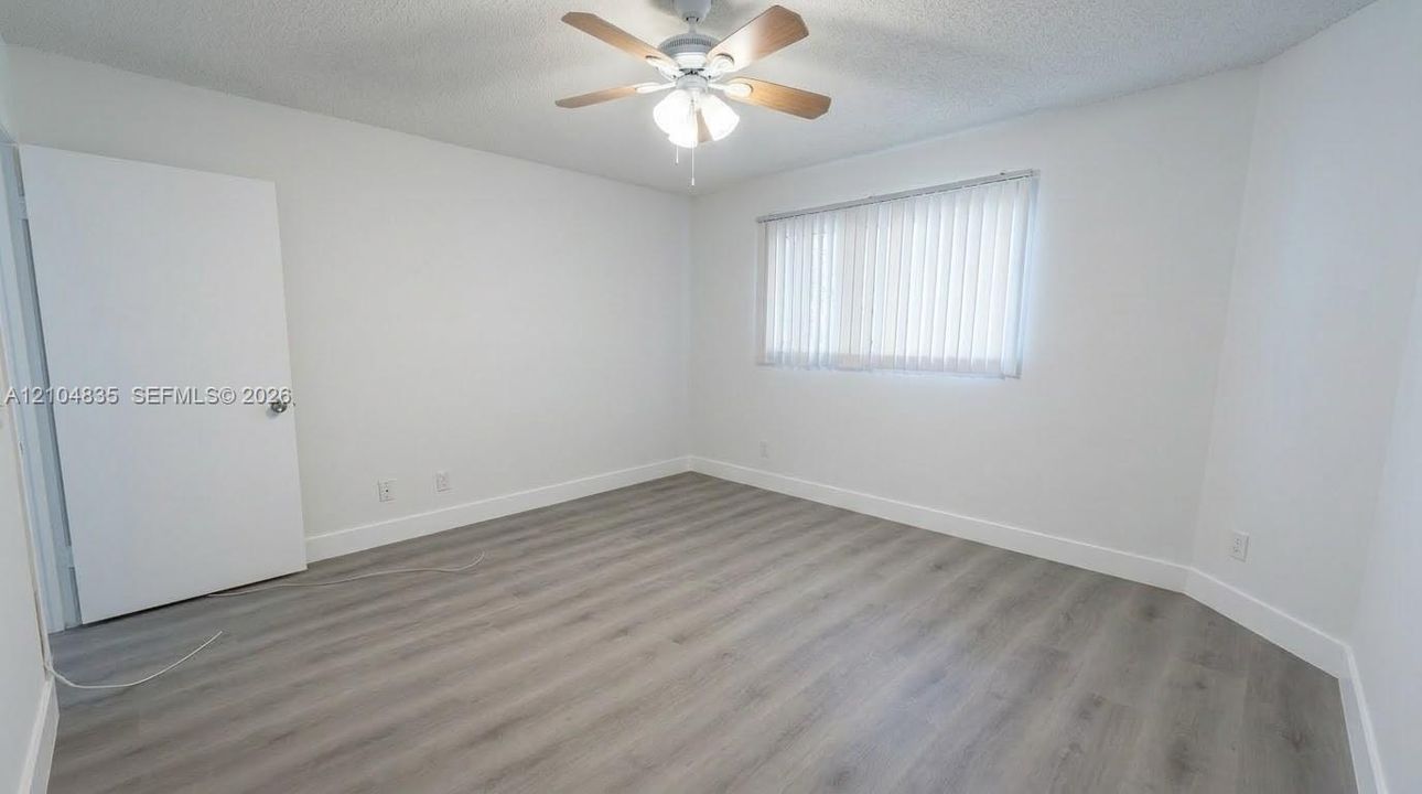 Neutral-toned interior featuring wood-finish flooring, a ceiling fan with integrated lighting, and vertical window blinds