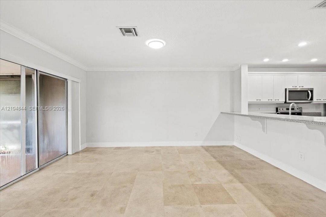 Open floor plan featuring large-format stone-finish flooring, white cabinetry, a breakfast bar with stone countertops, and sliding glass doors