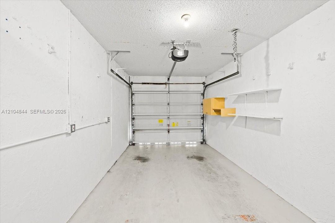 Single-car garage featuring a motorized door opener, concrete flooring, and built-in wall-mounted shelving